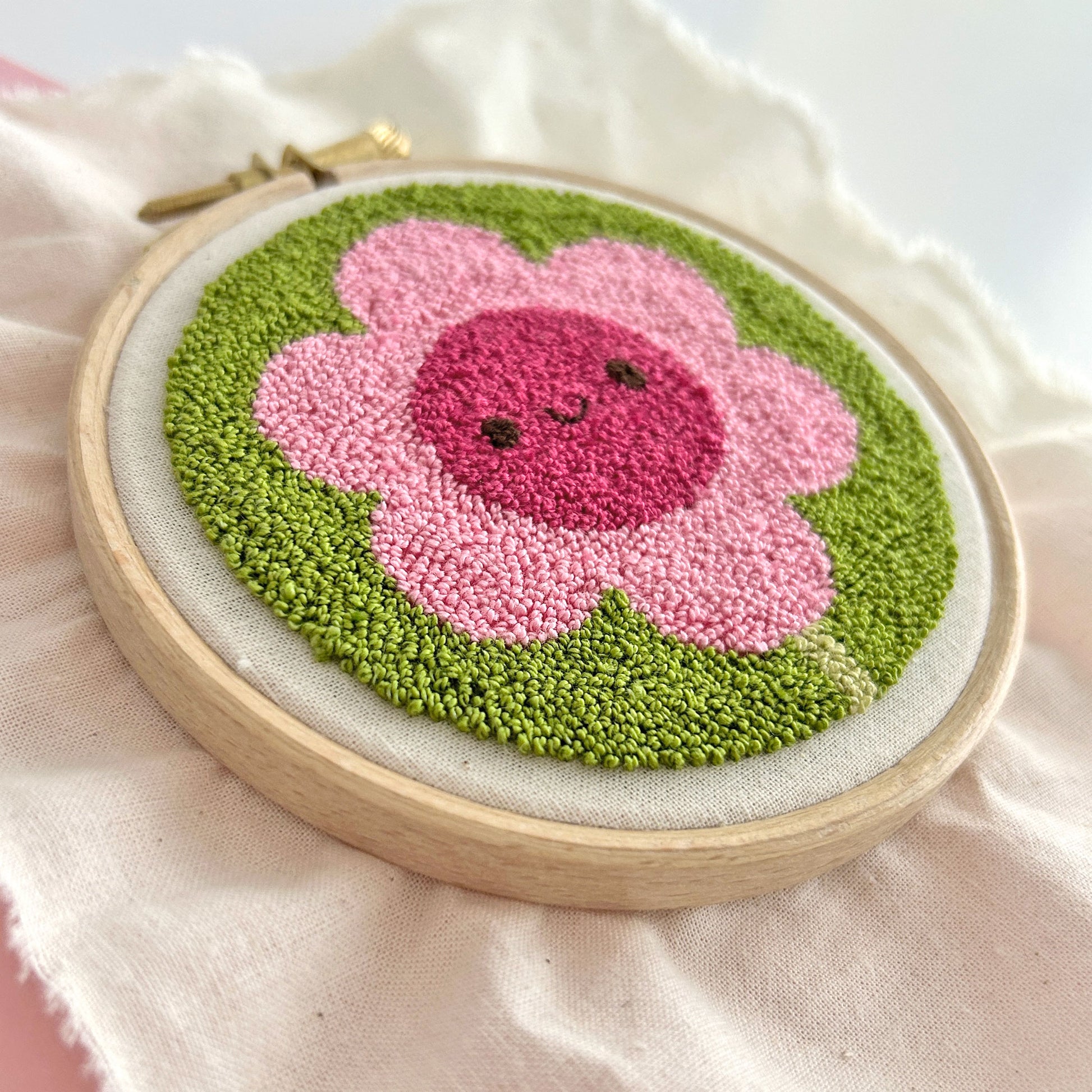 Miniature punch needle flower in hoop, alternate angle showing pile or loop stitch texture.