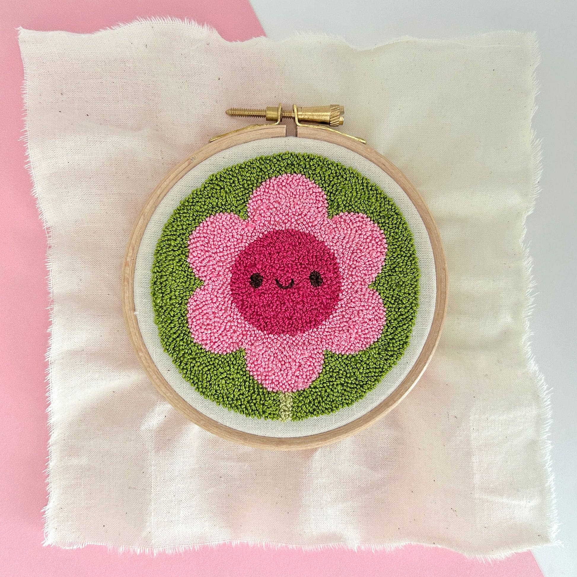 Finished miniature punch needle flower in embroidery hoop, showing pink petals and green background