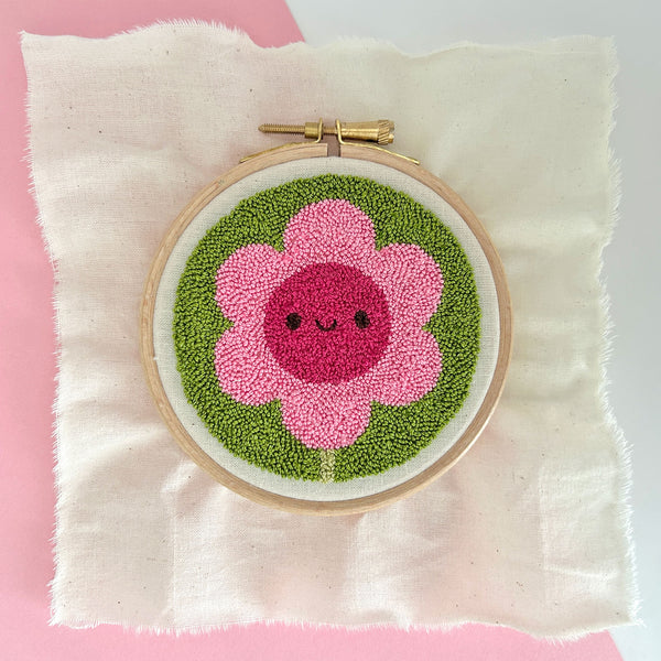 Finished miniature punch needle flower in embroidery hoop, showing pink petals and green background